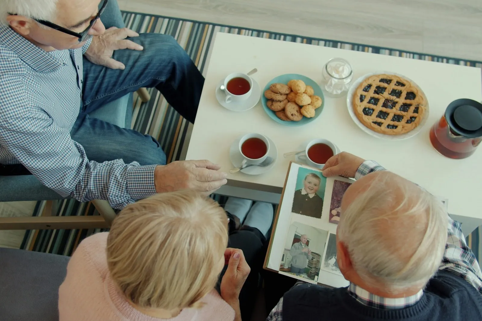Overhead view of a table with tea and pastries where several older people are looking at a photo album together.