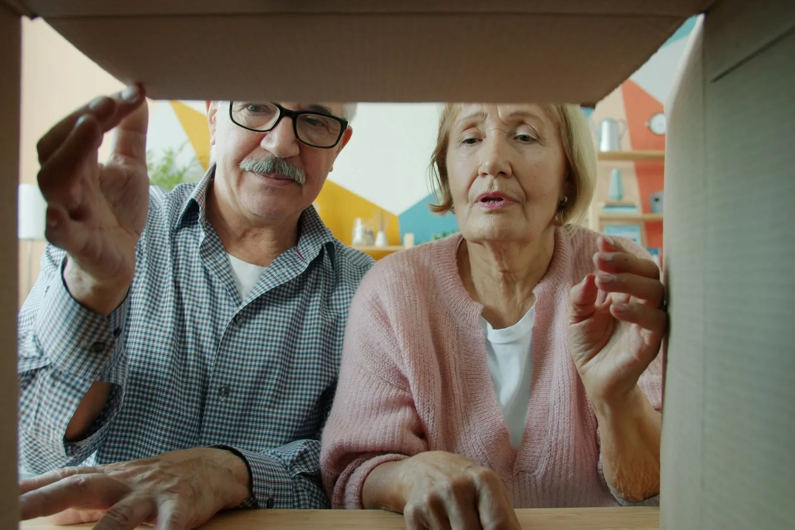 An older couple looking together into an opened cardboard moving box.