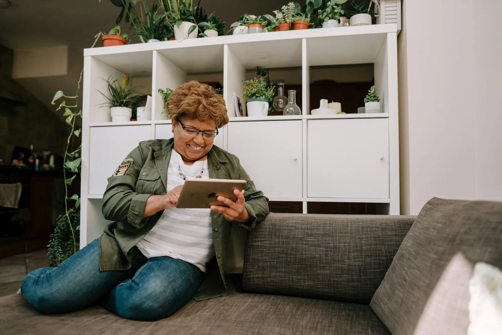 An older woman sitting comfortably on the floor by the sofa, looking at a tablet.