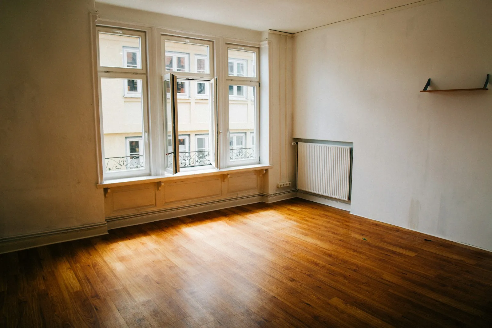 An emptied room with a parquet floor, white-painted walls and a wide multi-pane window.